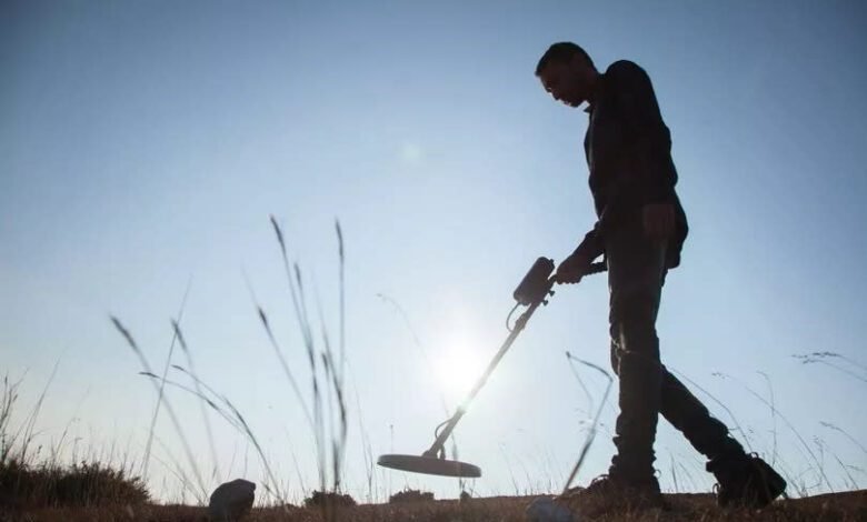 A silhouette of a man using a metal detector in a field